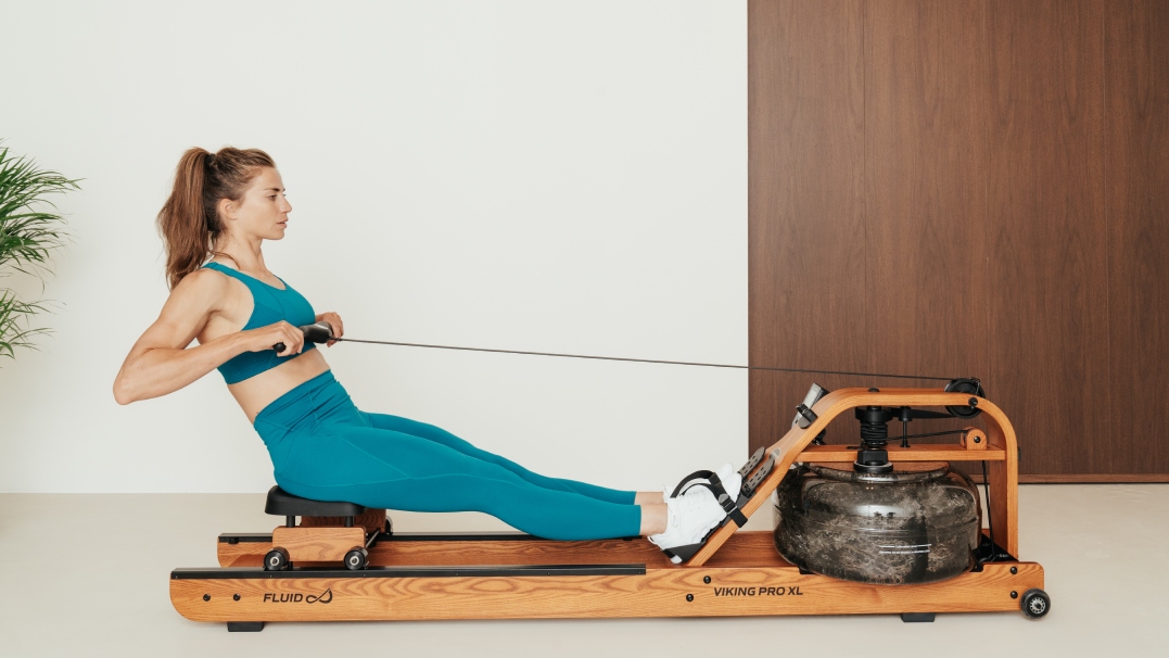 Een vrouw traint geconcentreerd haar armspieren op een houten roeiapparaat van Tunturi.